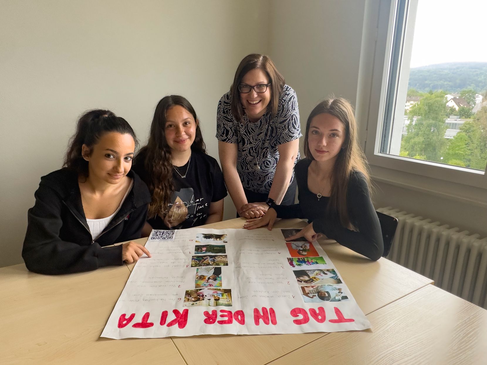 Vier Frauen unterschiedlichen Alters sitzen und stehen an einem Tisch.